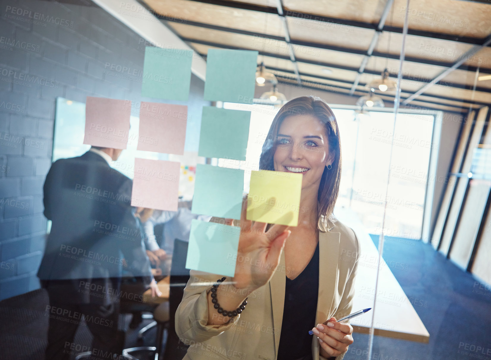 Buy stock photo Shot of a businesswoman arranging sticky notes on a glass wall during a brainstorming session