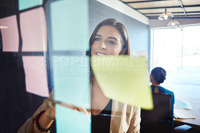 Buy stock photo Shot of a businesswoman arranging sticky notes on a glass wall during a brainstorming session