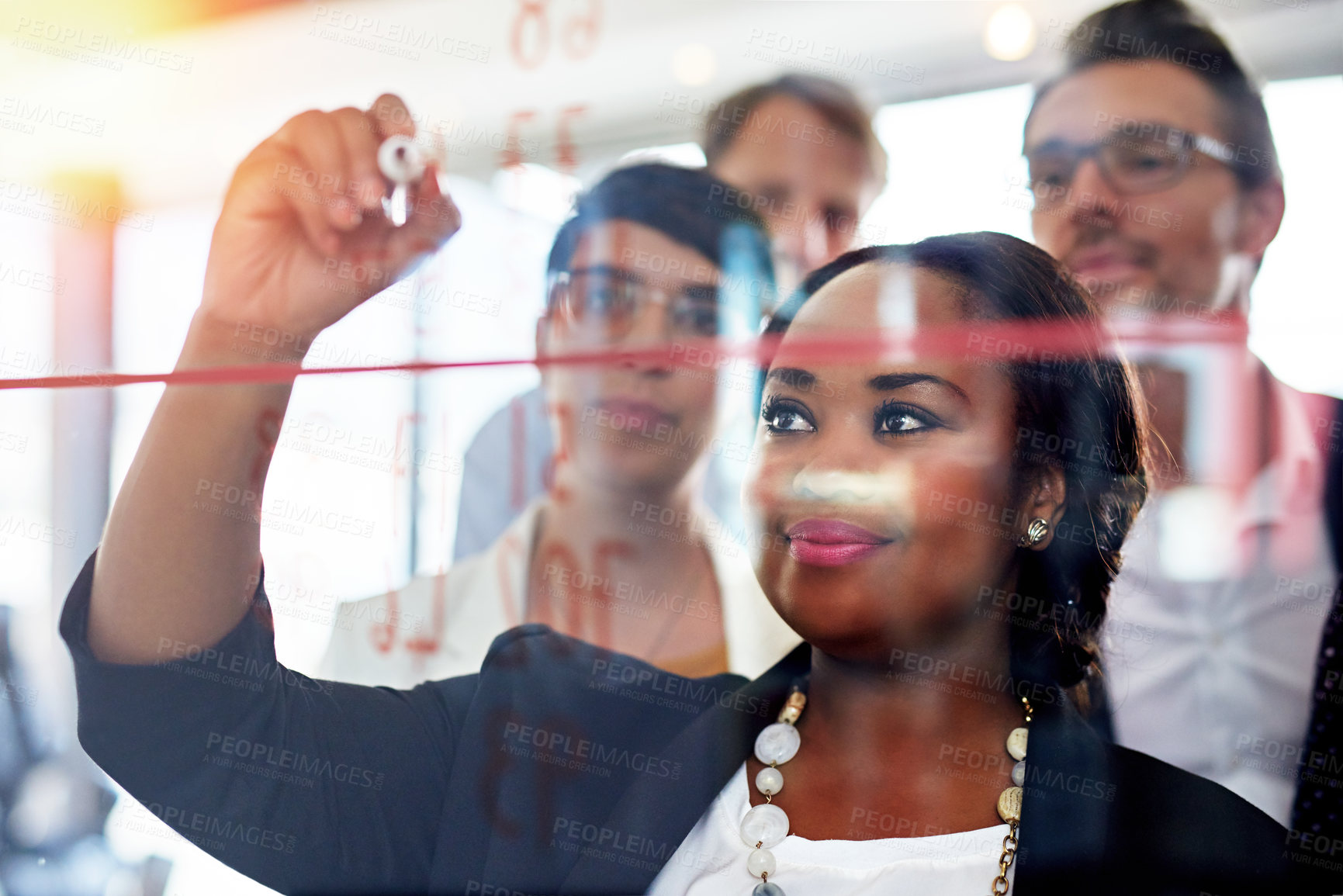 Buy stock photo Cropped shot of a businesswoman writing on a glass wall while her colleagues look on