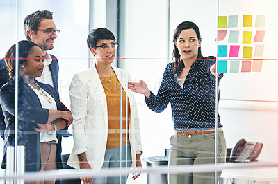 Buy stock photo Cropped shot of a businesswoman pointing out something on a glass wall while her colleagues look on