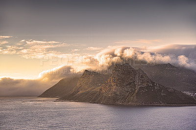 Buy stock photo Panorama of a mountain coastline with a cloudy sunset in South Africa. Scenic landscape of soft white clouds covering Table Mountain at dusk near a calm peaceful sea at Hout Bay near Cape Town.