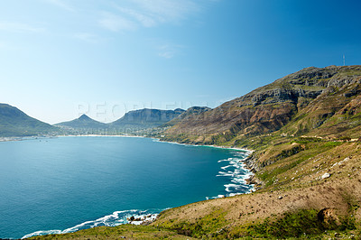 Buy stock photo Landscape of rocky coastline near mountains in South Africa for a peaceful nature scene. Large blue lake or calm sea surrounded by vibrant green hills against a clear sky in Hout Bay.