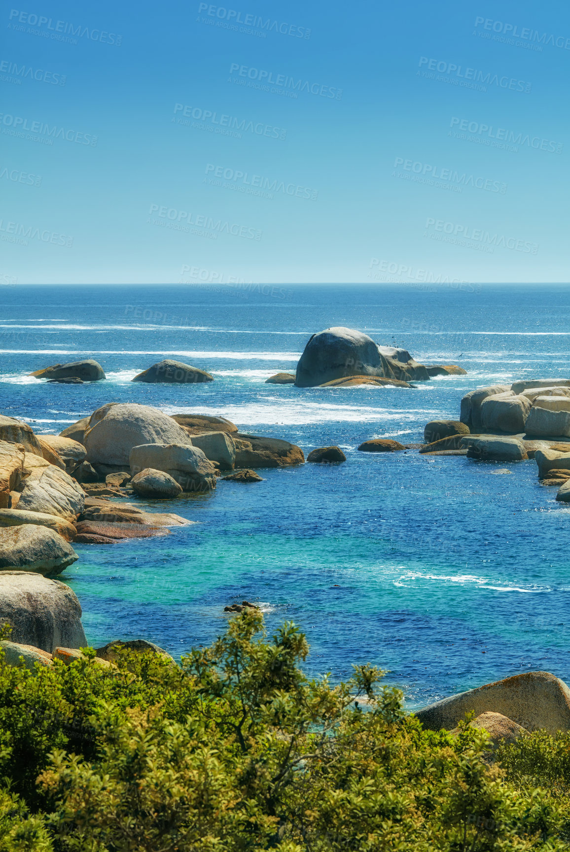 Buy stock photo Landscape of many rocks in the ocean surrounded by green bushes or shrubs. Large stones in a wide empty sea. Smooth rocks of various shapes lying in blue water near coastal area in Hout Bay