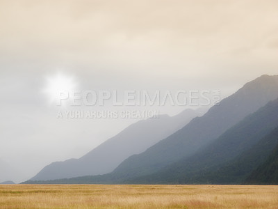 Buy stock photo Scenic view landscape of dry grassland or meadow with mountains or hills in the background with copyspace. Scenery of mother nature, sun shining and overcast cloudscape in the early morning