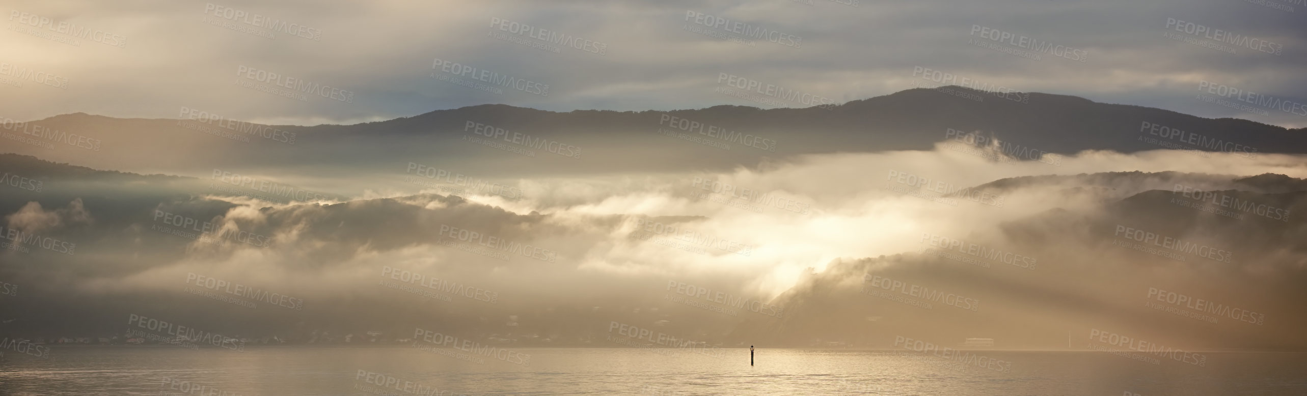 Buy stock photo Sunrise breaking through thick clouds over a calm body of water. Still, tranquil ocean in early morning. Concept of calm before the storm, rays peaking through clearing clouds with sky copyspace