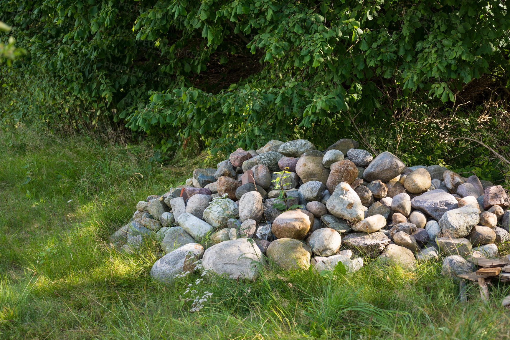 Buy stock photo Stacked large stones or rocks on a field of green grass. Rocks along a remote hiking trail in nature. Collected pile of stones marking forest ground, symbolising a small grave on a hiking trail 