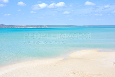 Buy stock photo A clear beach during summer with a cloudy sky. Blue ocean water at the seashore on a hot day. Beautiful tropical scenery or seascape with mountains in the background. Landscape vacation destination