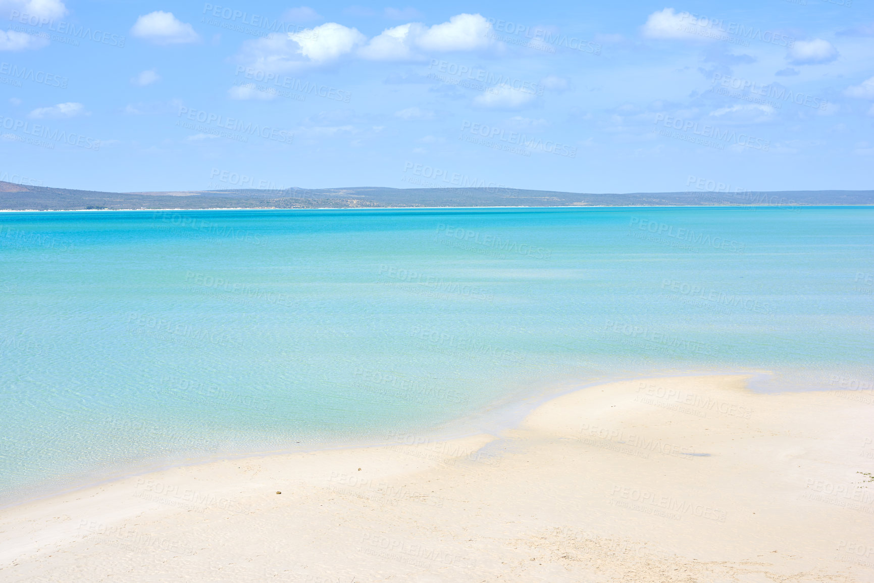 Buy stock photo A clear beach during summer with a cloudy sky. Blue ocean water at the seashore on a hot day. Beautiful tropical scenery or seascape with mountains in the background. Landscape vacation destination