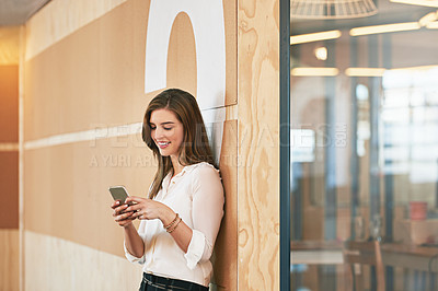 Buy stock photo Shot of a smiling young woman using her cellphone while standing in an office