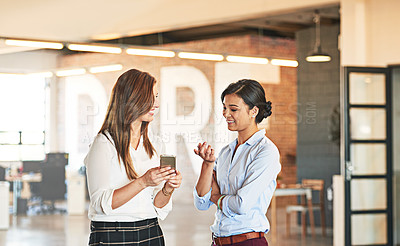 Buy stock photo Shot of two coworkers talking together over a cellphone while standing in an office