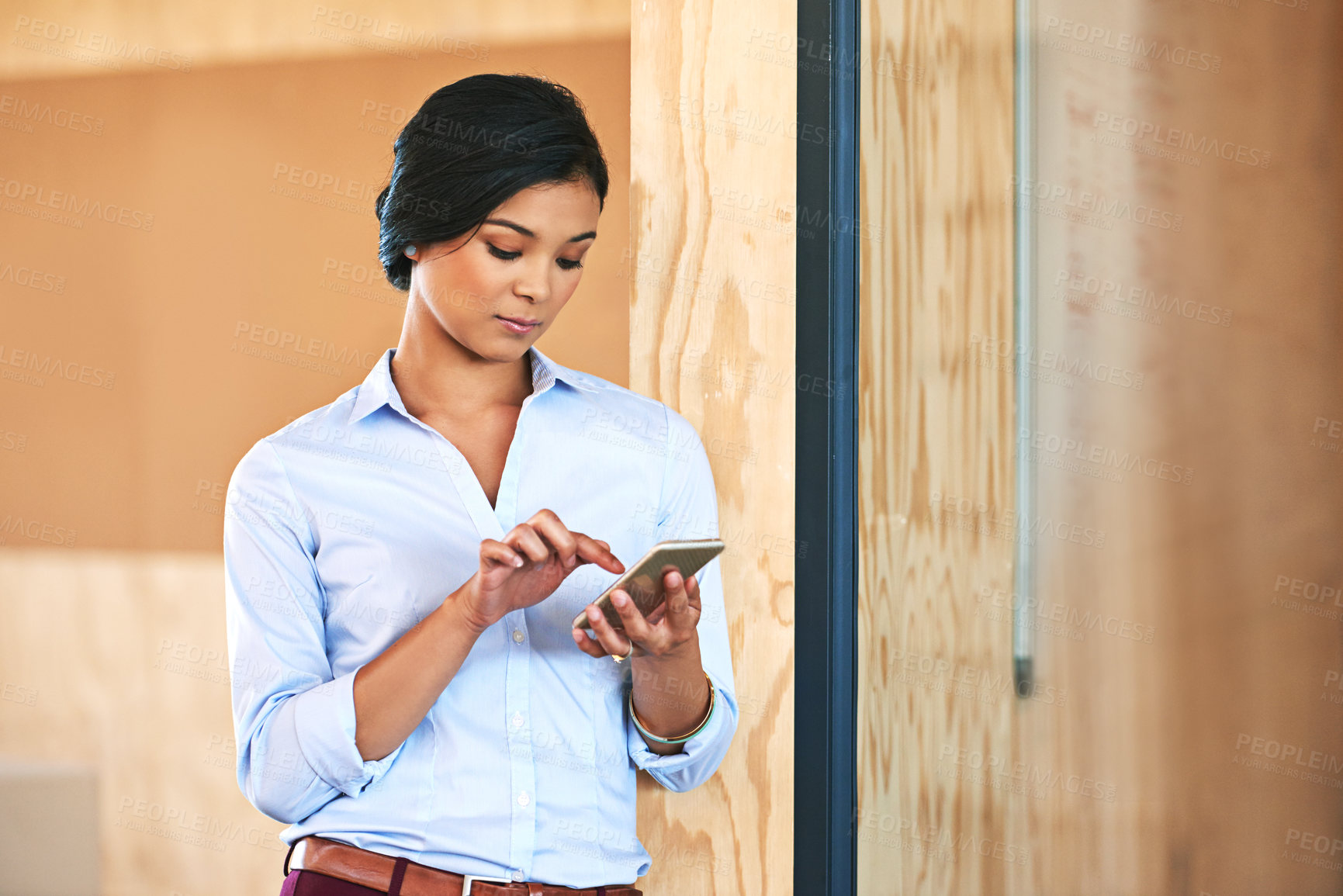 Buy stock photo Shot of a young woman using her cellphone while standing in an office