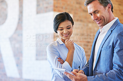 Buy stock photo Shot of a coworkers talking together over a notepad while standing in an office