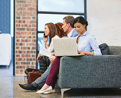 Buy stock photo Shot of a young businesswoman using a laptop while sitting with colleagues on a sofa