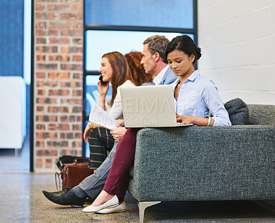 Buy stock photo Shot of a young businesswoman using a laptop while sitting with colleagues on a sofa