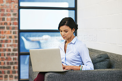 Buy stock photo Shot of a young businesswoman using a laptop while sitting on a sofa in an office