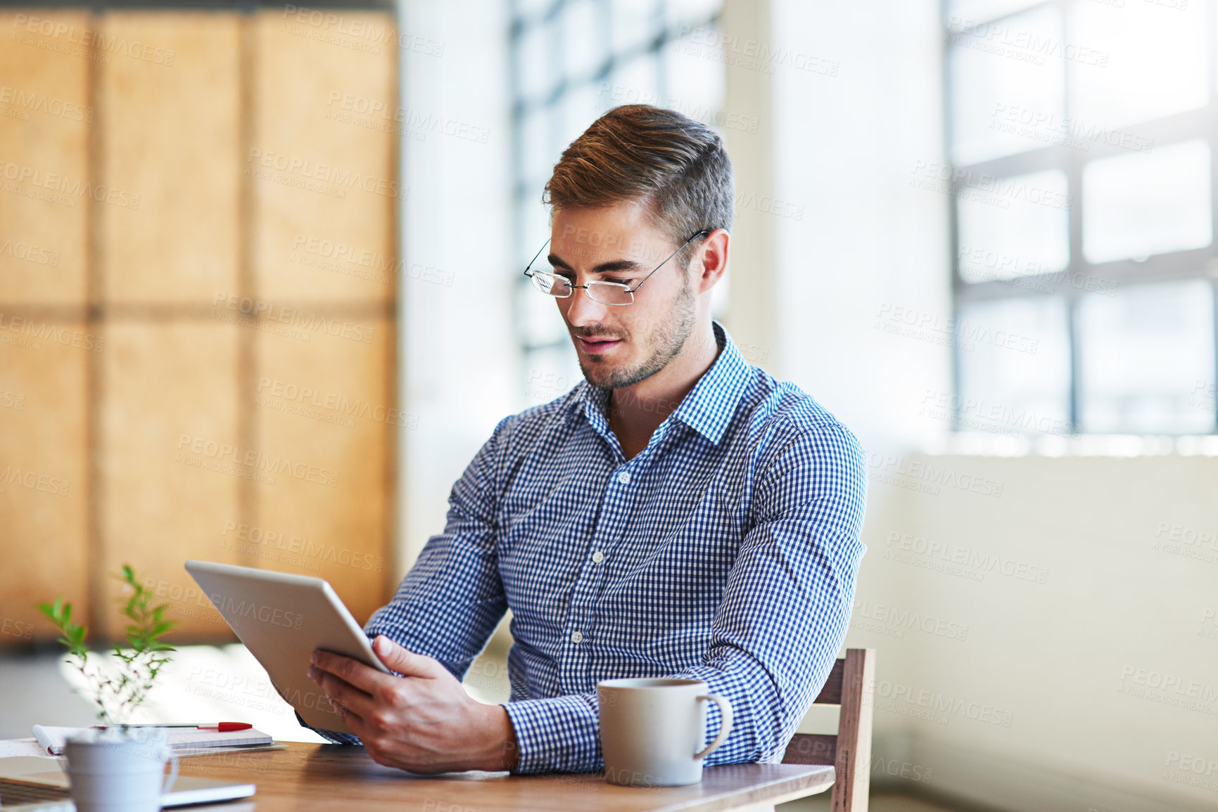 Buy stock photo Shot of a young businessman using a digital tablet in an office