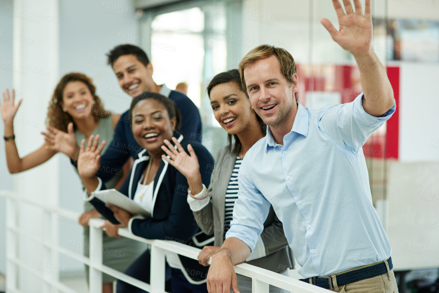 Buy stock photo Portrait of a group of smiling coworkers waving while leaning on a railing in an office