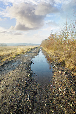 Buy stock photo A dirt road in the wet countryside by dry or arid grassland in early spring in Denmark. Empty gravel outdoors after heavy rain in the morning with a blue sky background. View of the countryside swamp