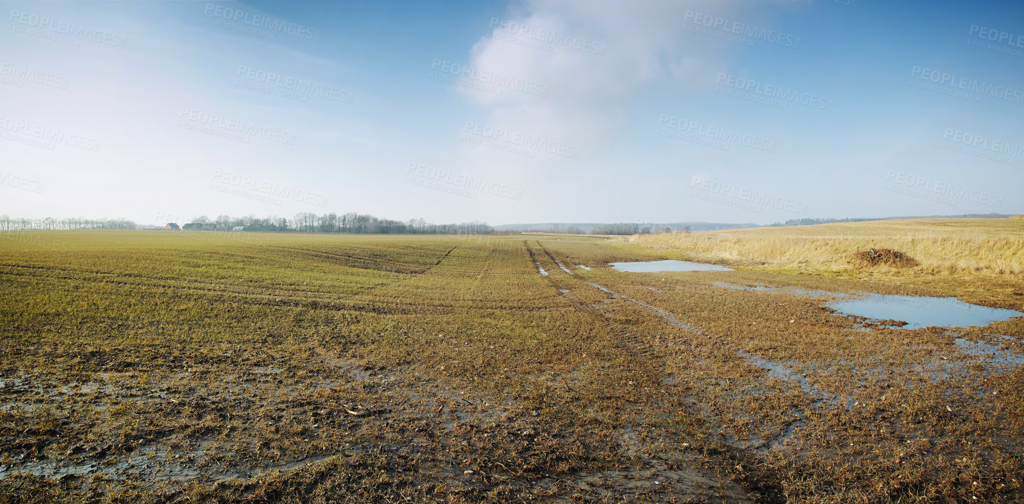 Buy stock photo Wet farmland in early spring in Jutland, Denmark. Grassland with puddles of water against cloudy blue sky. Agriculture field destroyed by water erosion damage on crop or grain in farmland after rain