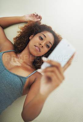 Buy stock photo High angle shot of a young woman looking at a cellphone while lying on the floor after yoga class