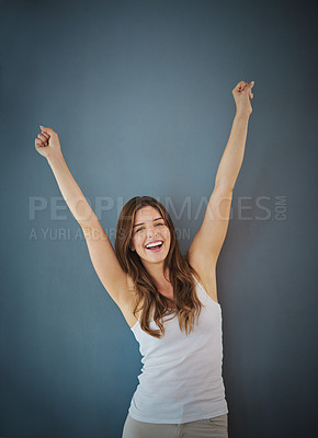 Buy stock photo Studio shot of a young woman raising her arms in triumph against a gray background