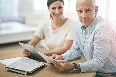 Buy stock photo Portrait of two coworkers sitting at a table discussing paperwork while using a digital tablet