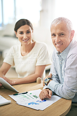 Buy stock photo Portrait of two coworkers sitting at a table discussing paperwork while using a digital tablet