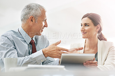 Buy stock photo Shot of two coworkers sitting at a table using a digital tablet