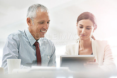 Buy stock photo Shot of two coworkers sitting at a table using a digital tablet