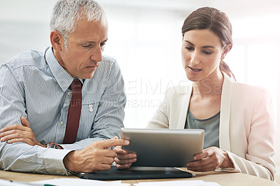 Buy stock photo Shot of two coworkers sitting at a table using a digital tablet