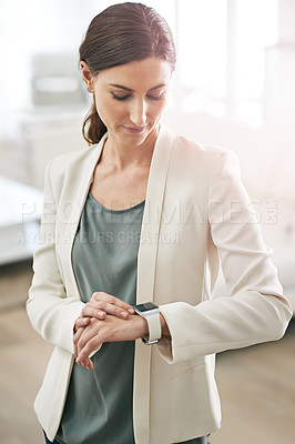 Buy stock photo Shot of a young businesswoman standing in an office using a smartwatch