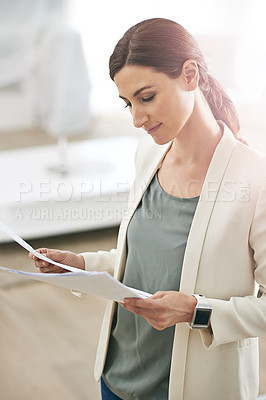 Buy stock photo Shot of a young businesswoman standing in her office reading paperwork