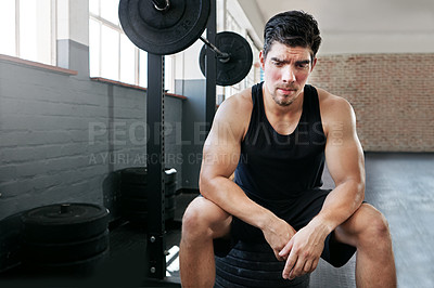 Buy stock photo Shot of a young man taking a break from working out with weights in the gym