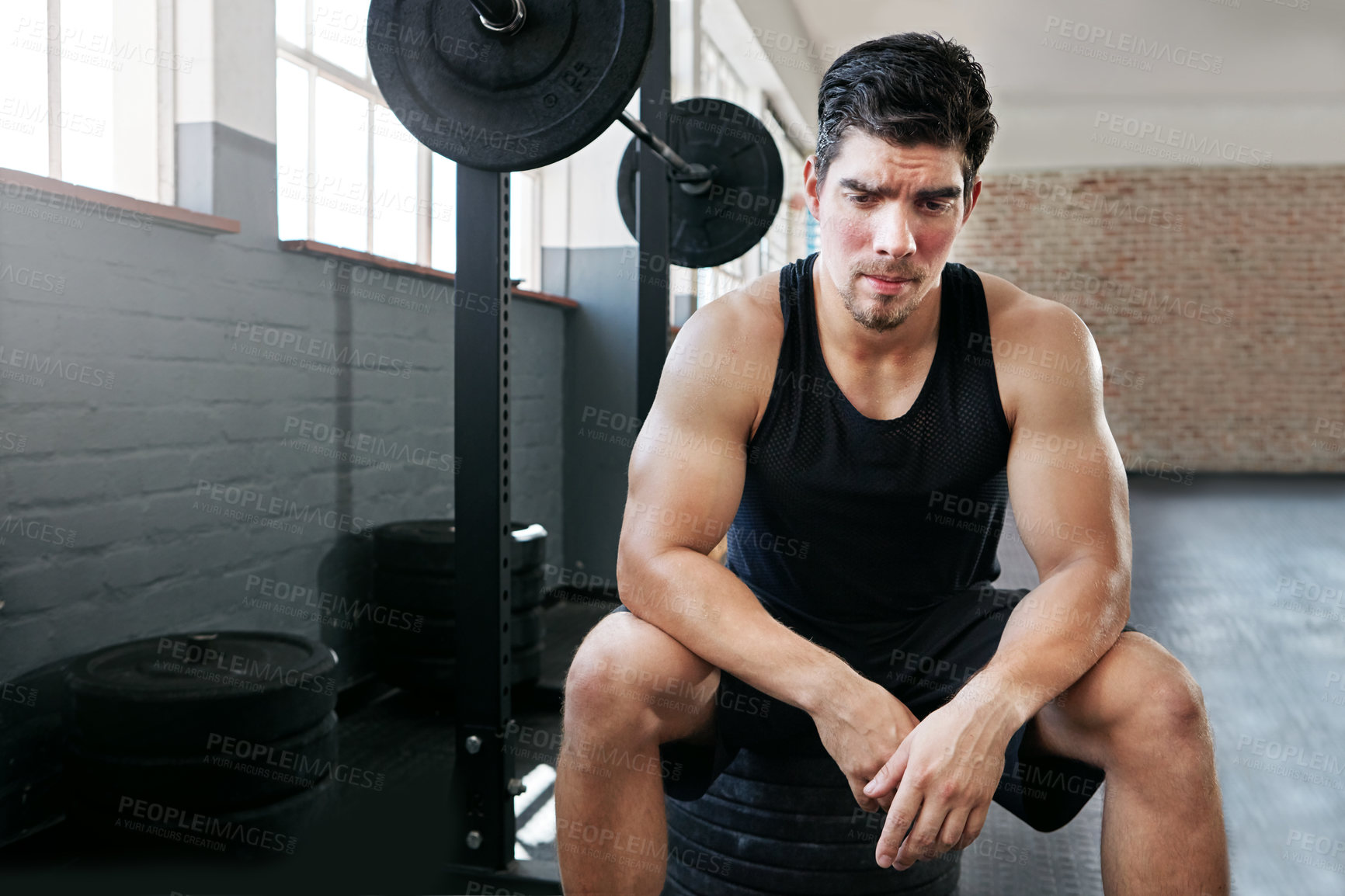 Buy stock photo Shot of a young man taking a break from working out with weights in the gym