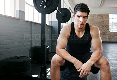 Buy stock photo Shot of a young man taking a break from working out with weights in the gym