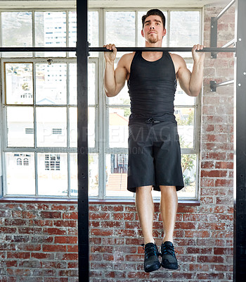 Buy stock photo Shot of a young man doing pull ups in a gym