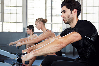 Buy stock photo Shot of a group of people working out on rowing machines in a gym