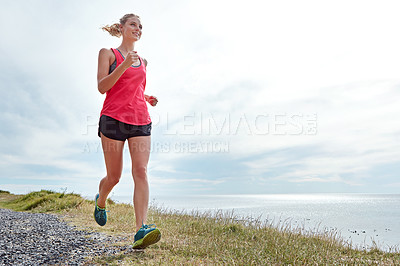 Buy stock photo Shot of a young woman jogging near the ocean
