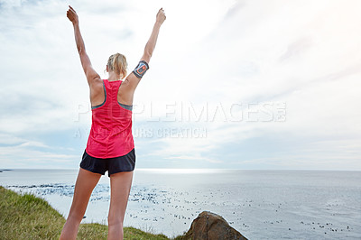 Buy stock photo Rearview shot of a woman with her arms raised in victory while out jogging by the ocean