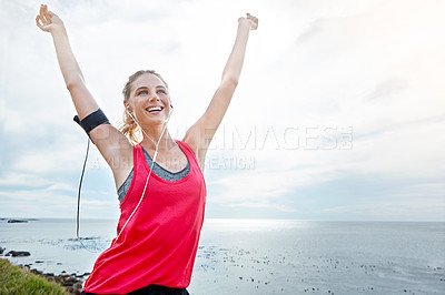 Buy stock photo Shot of a woman with her arms raised in victory while out jogging by the ocean
