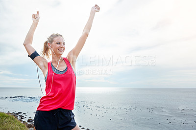Buy stock photo Shot of a woman with her arms raised in victory while out jogging by the ocean