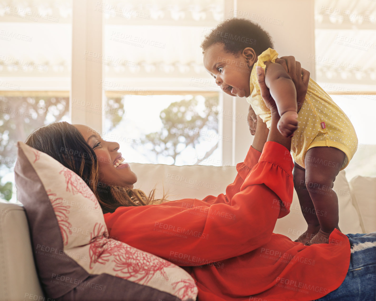 Buy stock photo Shot of a mother holding up her baby while lying on her sofa at home