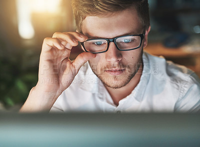 Buy stock photo Shot of a young designer adjusting his glasses as he looks at his computer screen