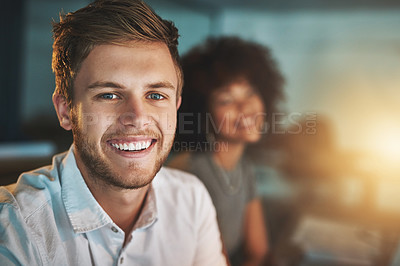 Buy stock photo Shot of a young designer working late with his colleague blurred in the background