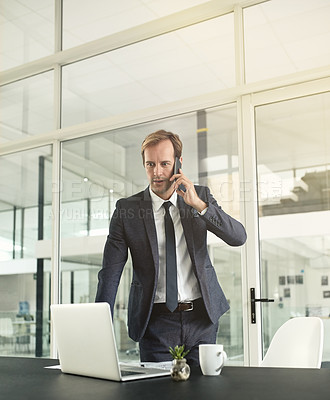 Buy stock photo Shot of a businessman talking on his cellphone while using his laptop