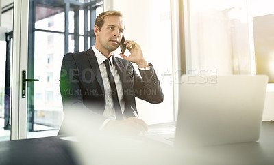 Buy stock photo Shot of a businessman talking on his cellphone with his laptop in front of him
