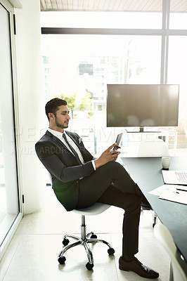 Buy stock photo Shot of a businessman using his tablet while sitting in an office