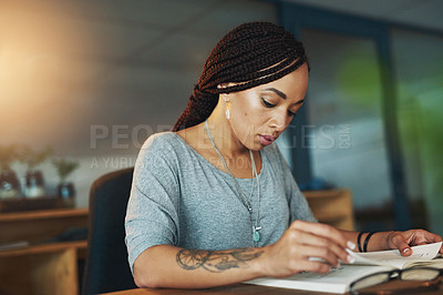 Buy stock photo Cropped shot of a young woman reading a book while working late in her office