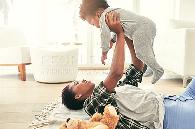 Buy stock photo Shot of a mother lying on the floor holding her little baby boy up in the air