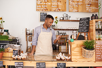 Buy stock photo Black man, coffee shop and store phone of an entrepreneur with happiness from small business. Cafe, mobile and barista looking at online app with a smile at bakery and restaurant feeling happy